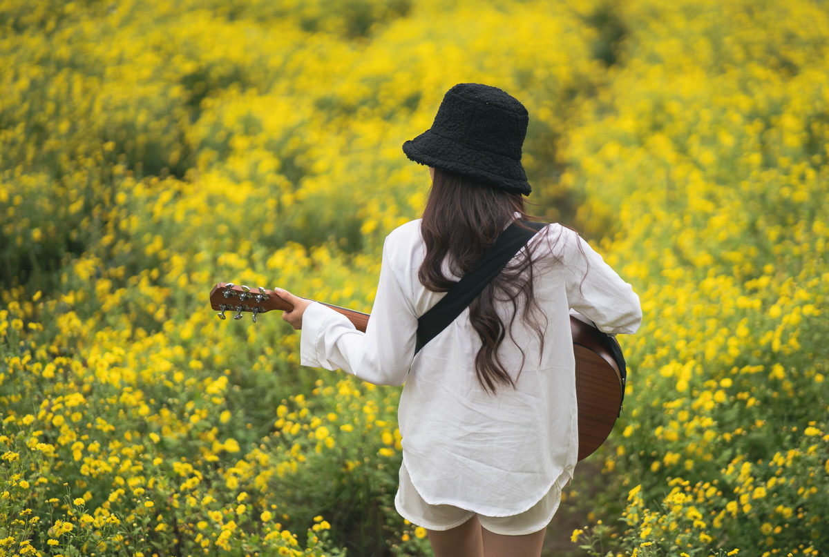 Asian young woman playing guitar and sing music in the park, asian woman palying guitar at yellow flowers garden