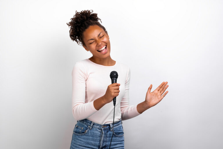 Funny mulatto woman singer holds a microphone in her hands against a ligth studio background